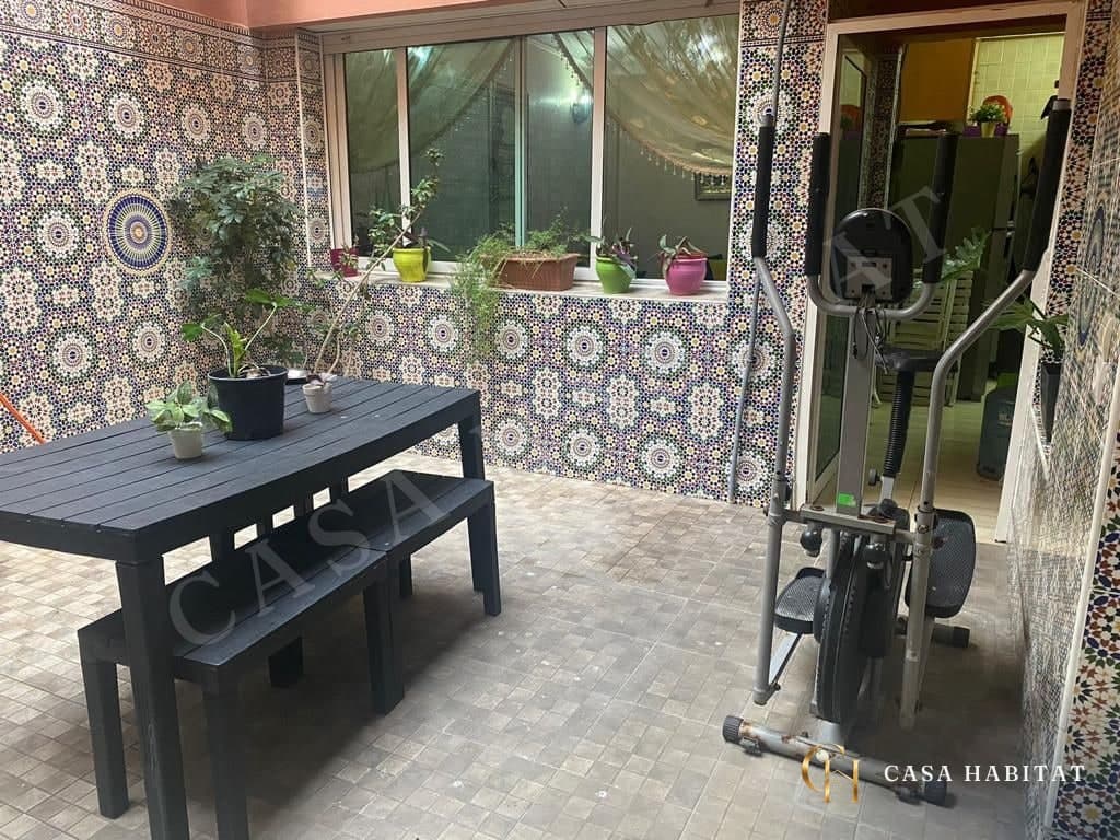 Terrasse carrelée avec table noire, bancs et vélo d'appartement