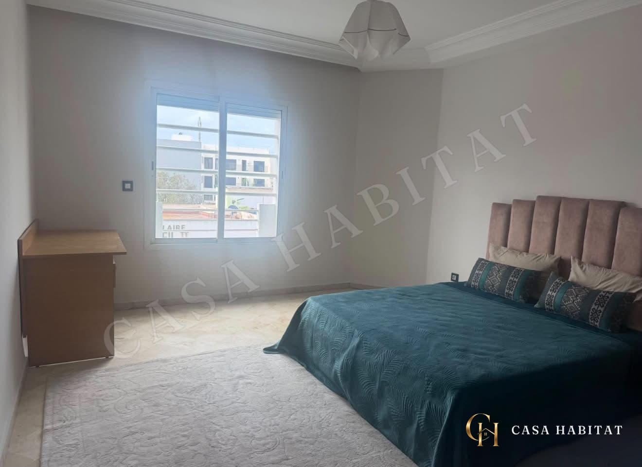 Chambre avec lit bleu sarcelle et fenêtre donnant sur immeubles