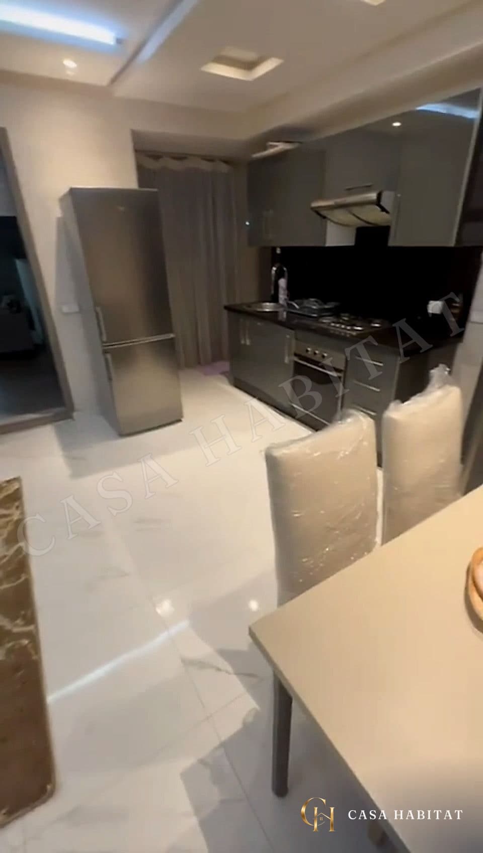 Cuisine grise avec réfrigérateur inox et table recouverte de housses