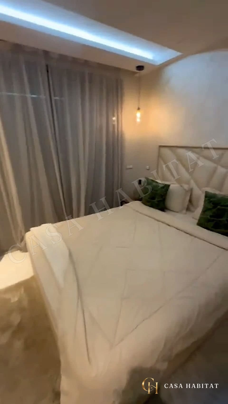 Chambre avec lit blanc, coussins verts et rideaux voilage