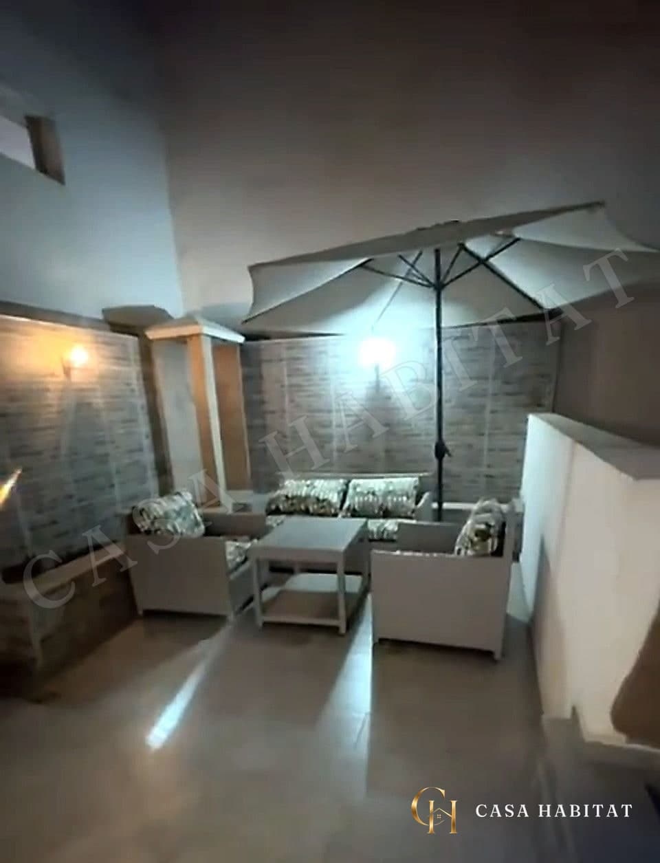 Terrasse avec fauteuils blancs, parasol et murs en briques