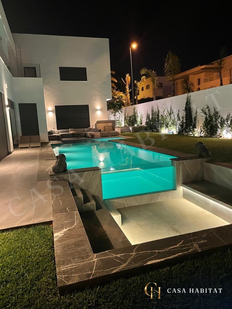 Piscine éclairée la nuit avec banquettes et sculptures de chiens