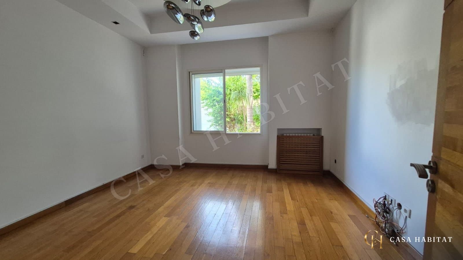 Chambre au parquet clair avec lustre chromé et fenêtre