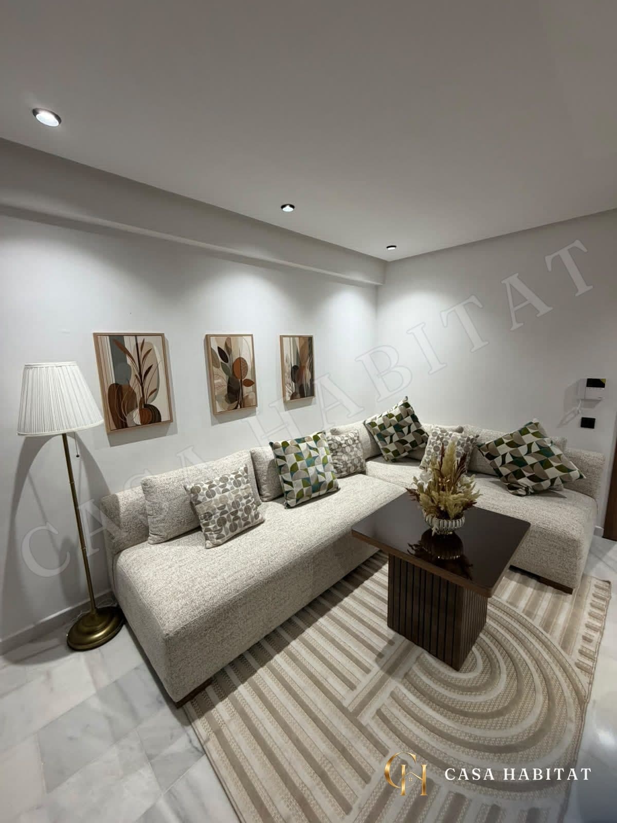Salon avec canapé d'angle beige, coussins colorés et tableaux muraux