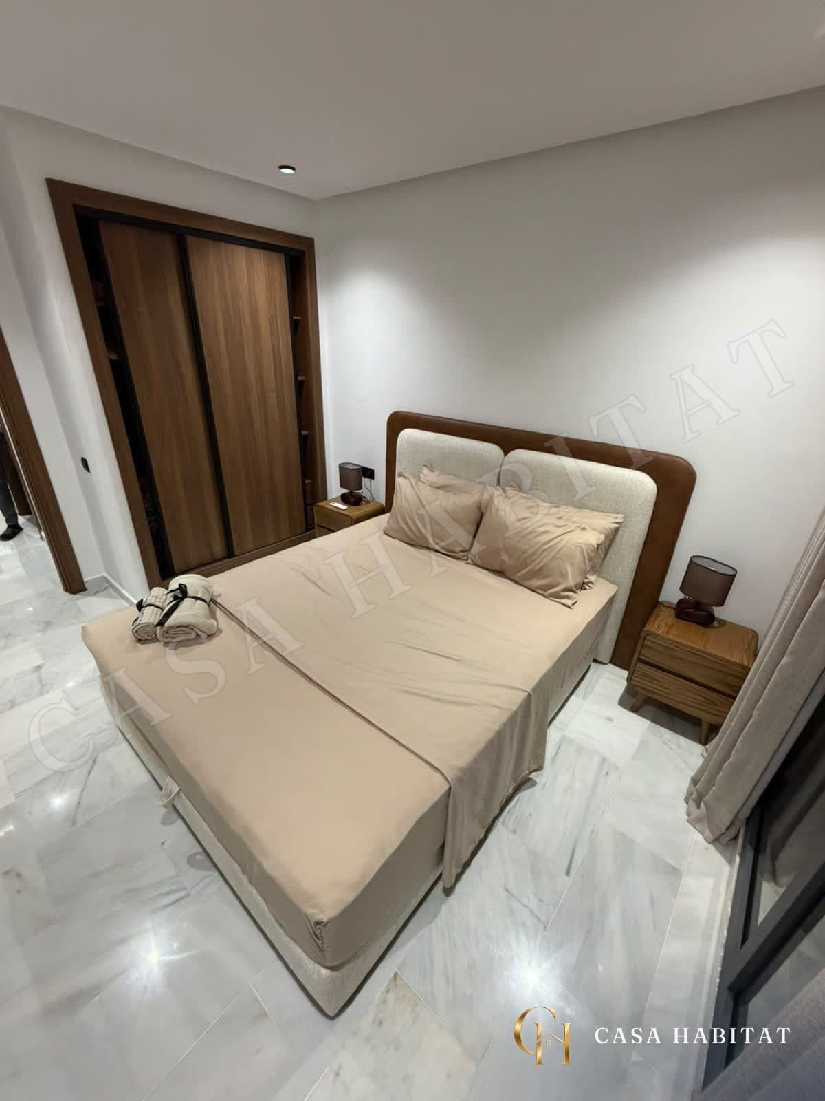 Chambre avec lit beige, placard en bois coulissant et tables de chevet