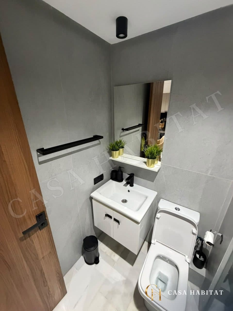 Toilettes avec lavabo blanc, miroir et étagère de plantes vertes