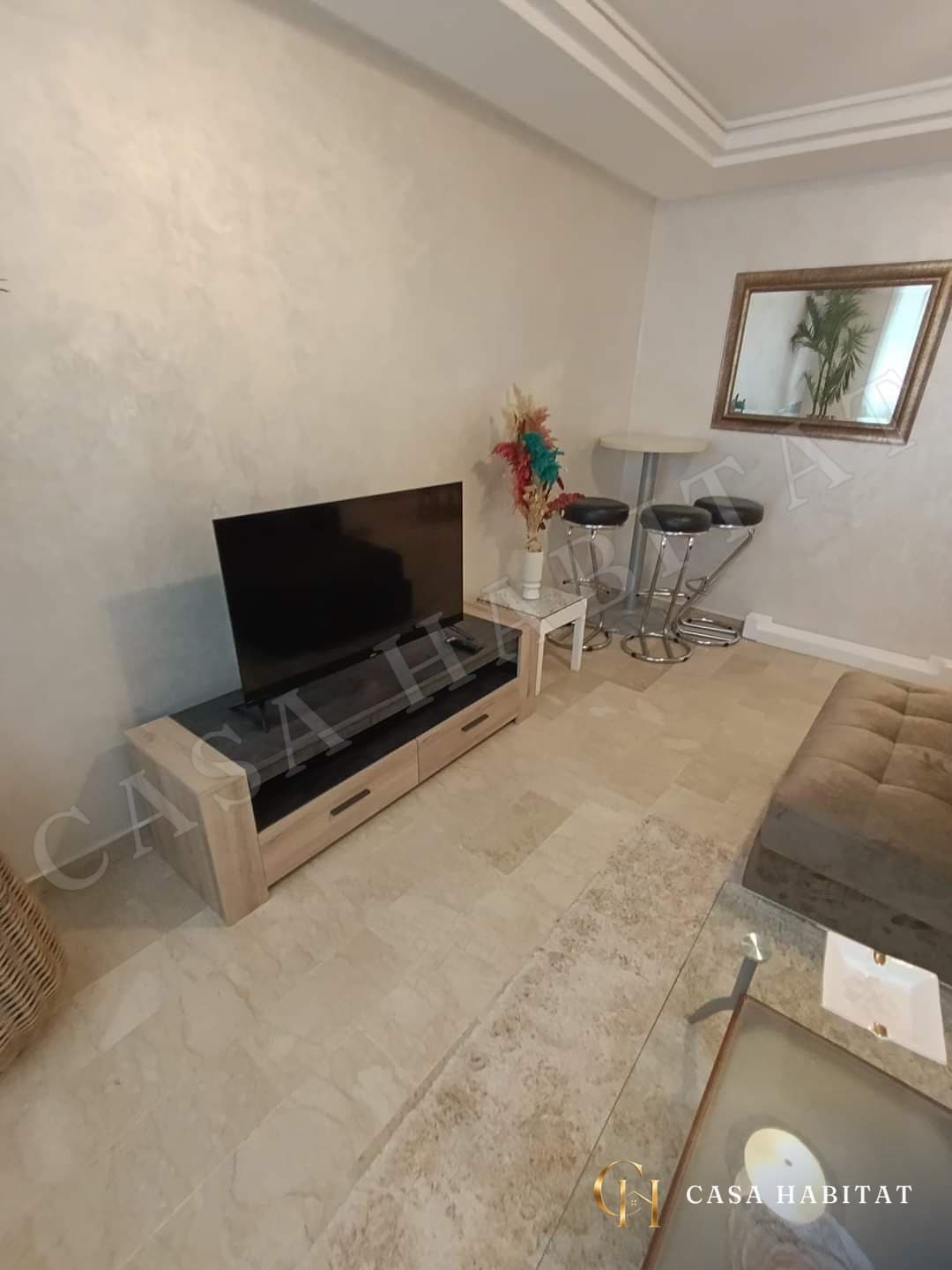 Salon avec meuble TV en bois clair, téléviseur et tabouret de bar