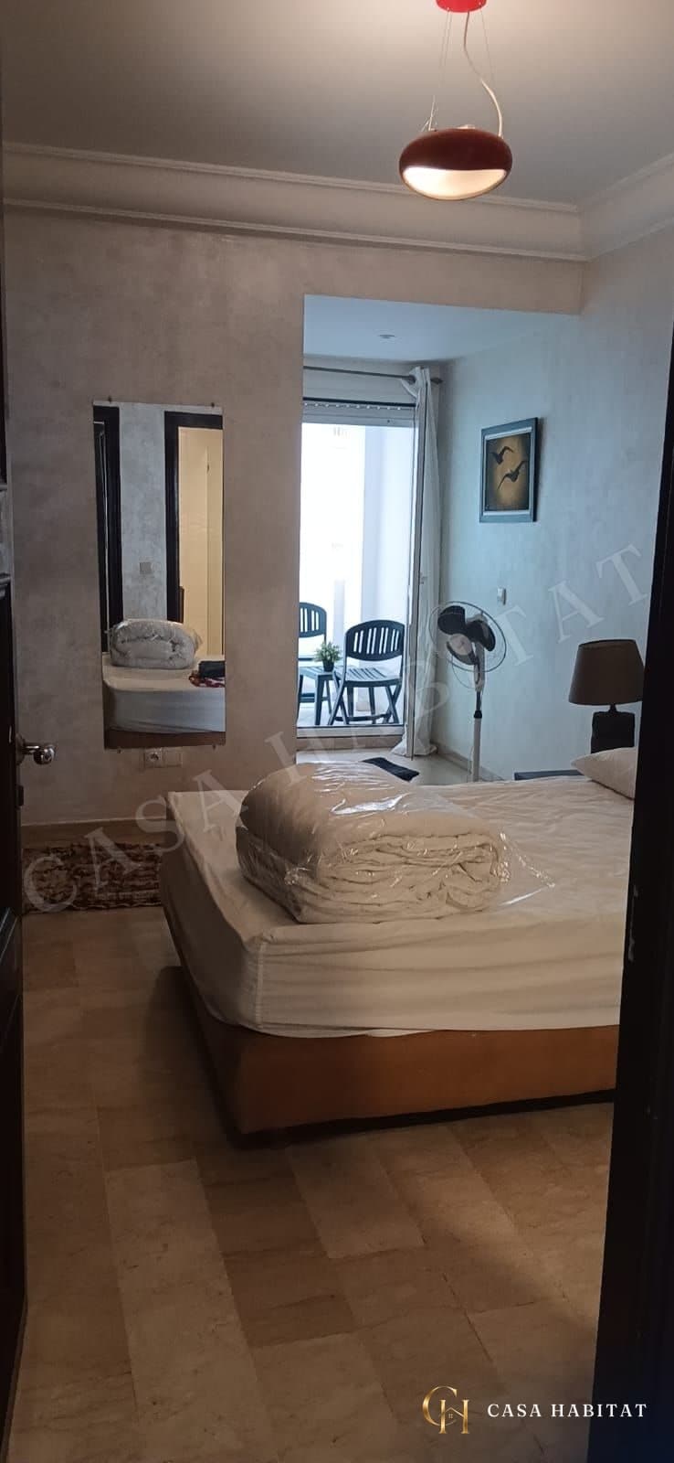 Chambre avec grand lit, miroir sur pied et fenêtre donnant sur balcon