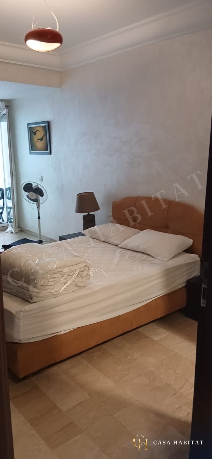 Chambre avec grand lit blanc, oreillers et ventilateur sur pied