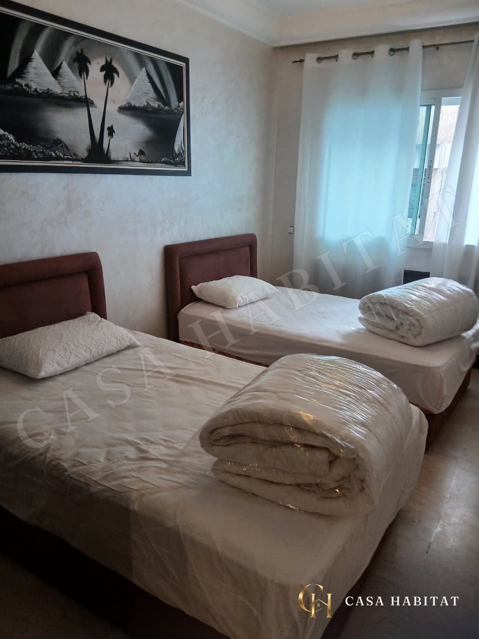 Chambre avec deux lits simples, tableau de pyramides et rideaux blancs