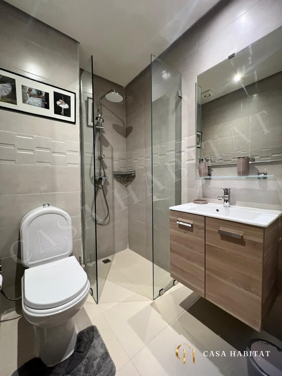 Salle de bain avec douche en verre, lavabo sur meuble bois et WC