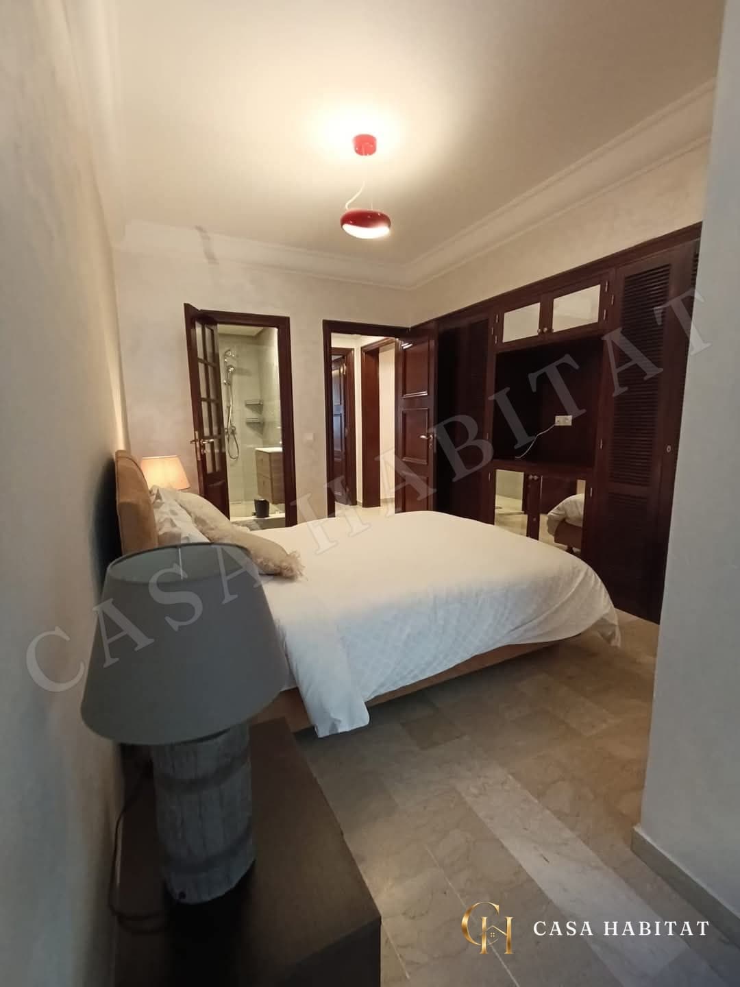 Chambre avec lit blanc, armoire en bois et lampe de chevet
