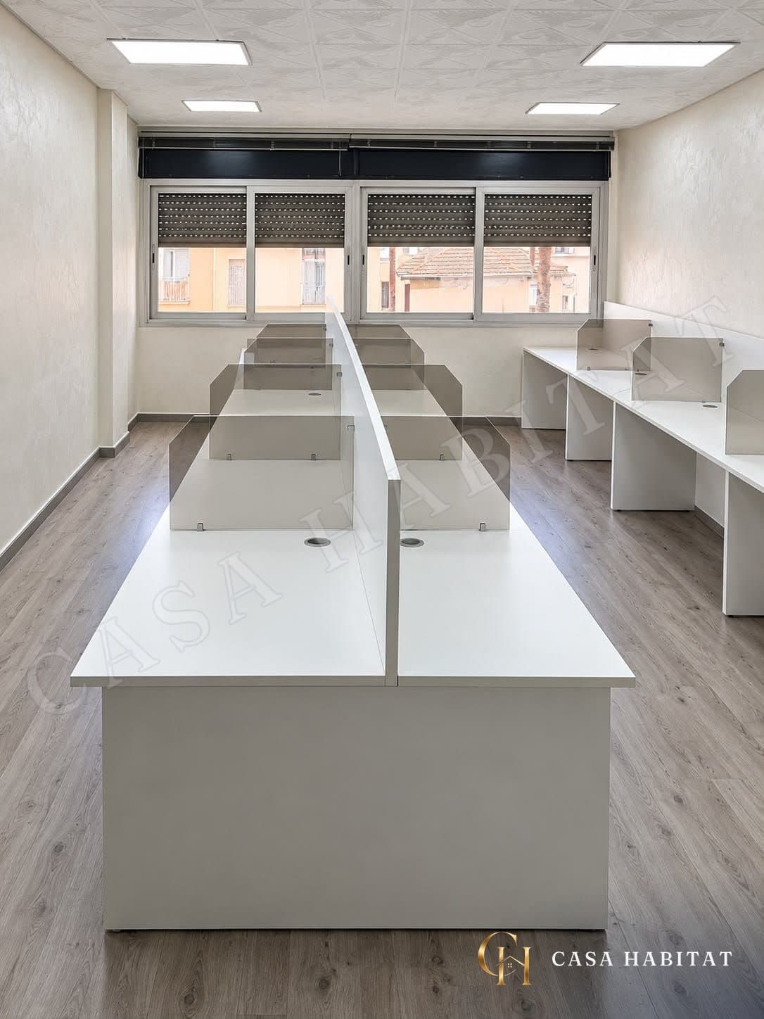 مساحة عمل مع مكاتب بيضاء، وفواصل زجاجية ونوافذ